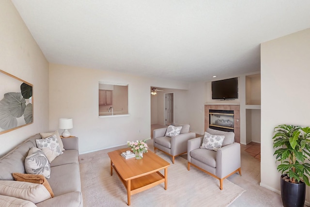 living area featuring light carpet, a tiled fireplace, a ceiling fan, and baseboards