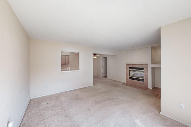 unfurnished living room with a fireplace, light colored carpet, a sink, ceiling fan, and baseboards