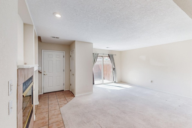 unfurnished living room with visible vents, a tile fireplace, tile patterned floors, carpet, and a textured ceiling