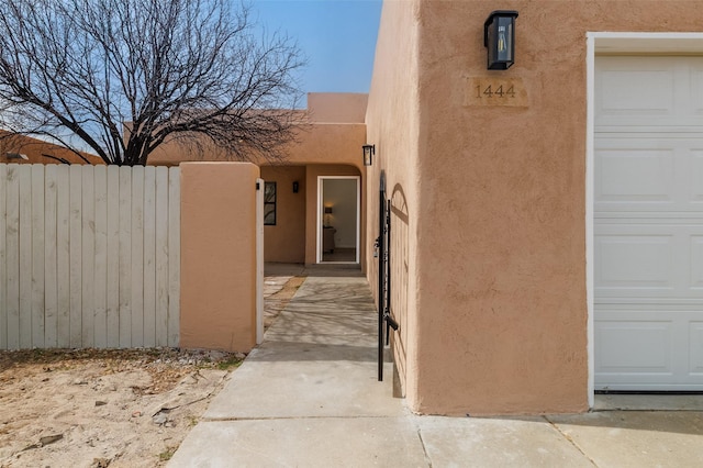 property entrance featuring a garage, fence, and stucco siding