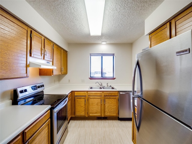 kitchen with brown cabinets, under cabinet range hood, stainless steel appliances, and a sink