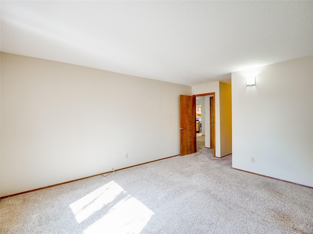 spare room with baseboards and light colored carpet