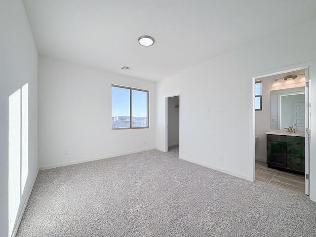 unfurnished bedroom with light carpet, visible vents, baseboards, ensuite bathroom, and a sink