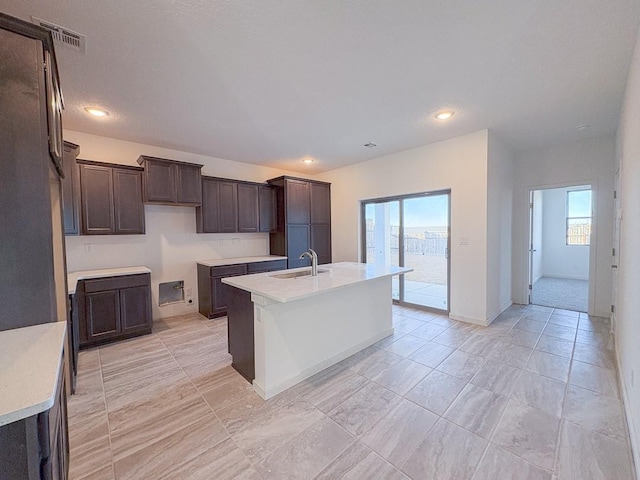 kitchen with visible vents, a kitchen island with sink, a healthy amount of sunlight, a sink, and dark brown cabinetry