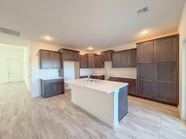 kitchen featuring a kitchen island with sink, visible vents, a sink, and dark brown cabinetry