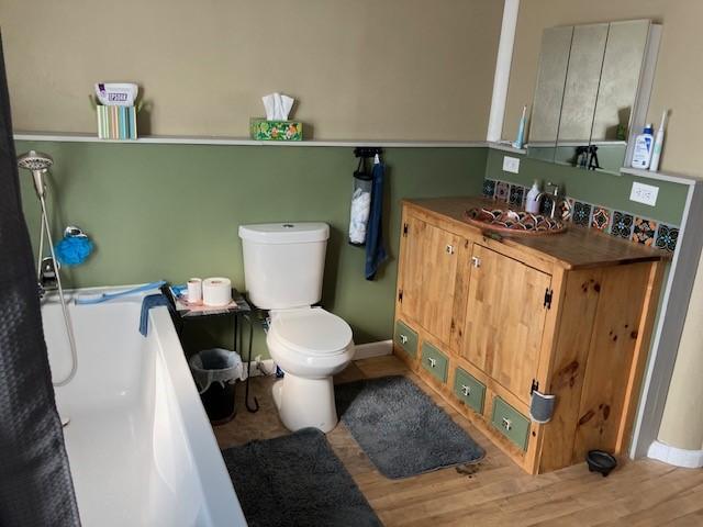 bathroom with baseboards, a washtub, toilet, wood finished floors, and vanity