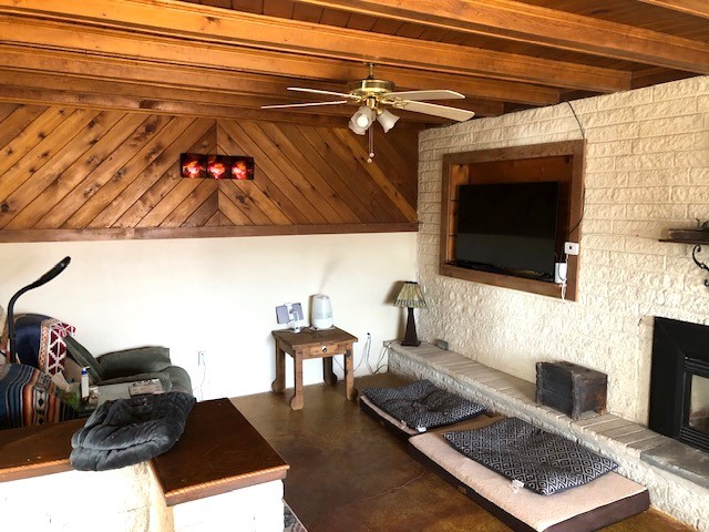 living room with a large fireplace, beamed ceiling, concrete flooring, and ceiling fan