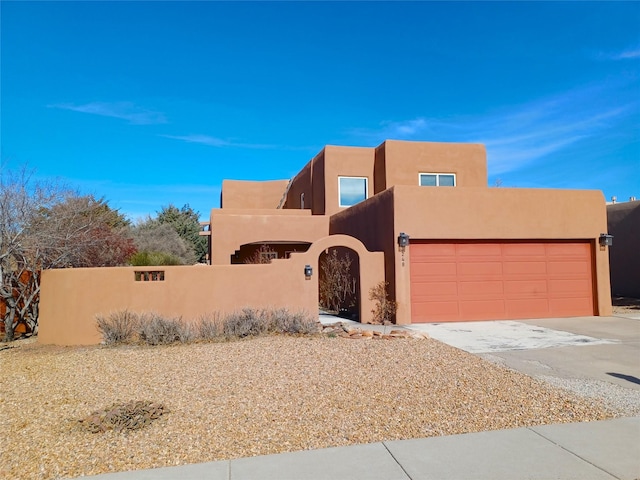 adobe home featuring concrete driveway, a fenced front yard, an attached garage, and stucco siding