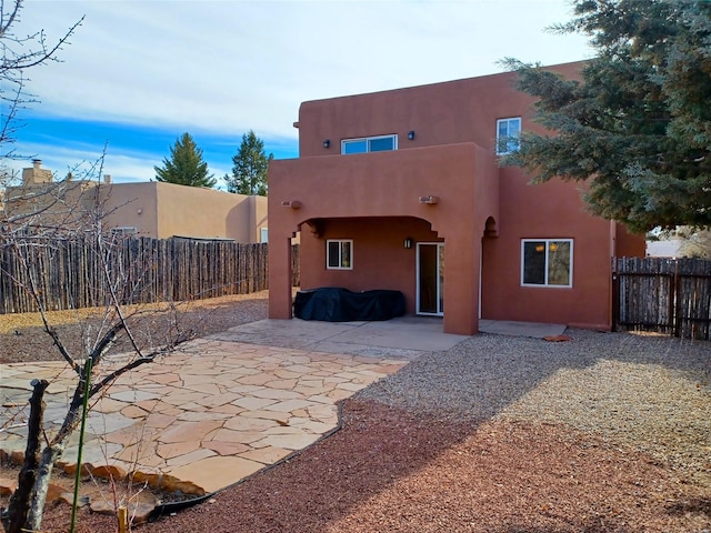 rear view of property featuring a patio area, fence, and stucco siding