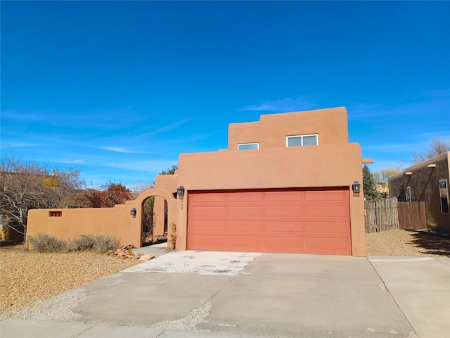 pueblo-style house featuring driveway, fence, a gate, and stucco siding