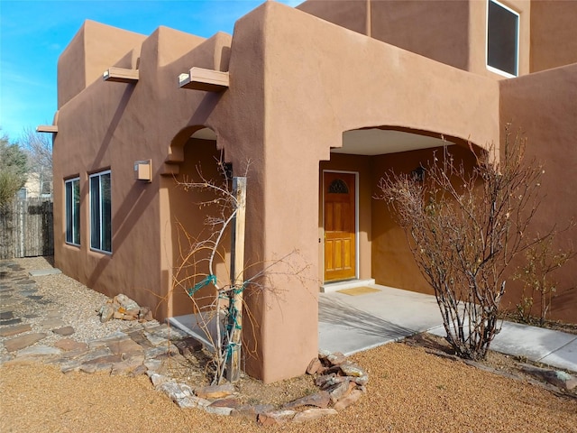 view of exterior entry with fence and stucco siding