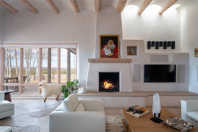 living room with a towering ceiling, a lit fireplace, and beam ceiling