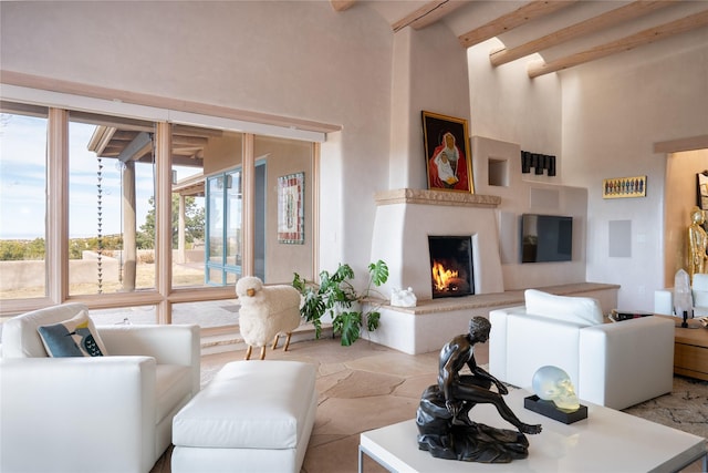 living area with a towering ceiling, a warm lit fireplace, stone finish flooring, and beamed ceiling