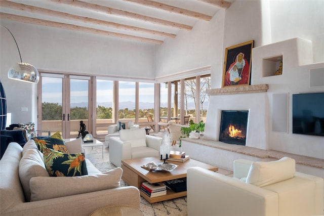 living room with a warm lit fireplace, beamed ceiling, a high ceiling, and french doors