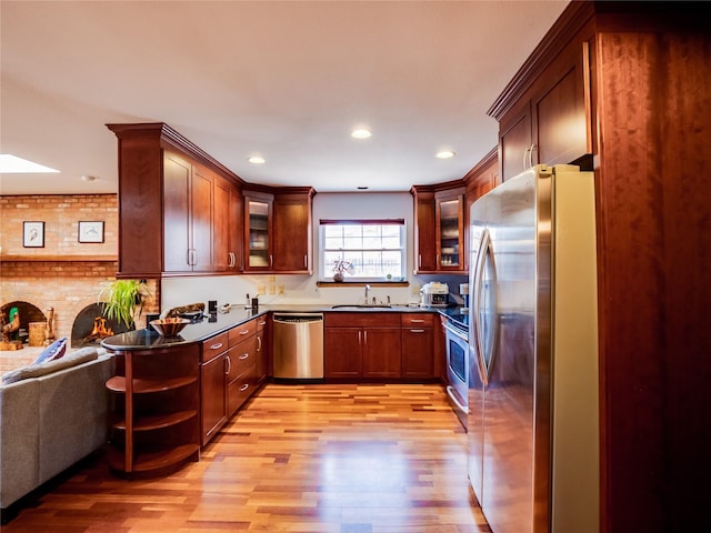 kitchen featuring a sink, open floor plan, appliances with stainless steel finishes, light wood-type flooring, and glass insert cabinets