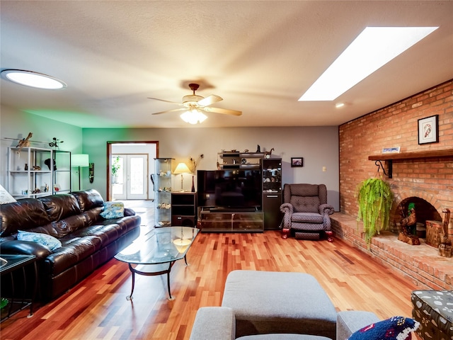 living room featuring a skylight, a brick fireplace, ceiling fan, and wood finished floors