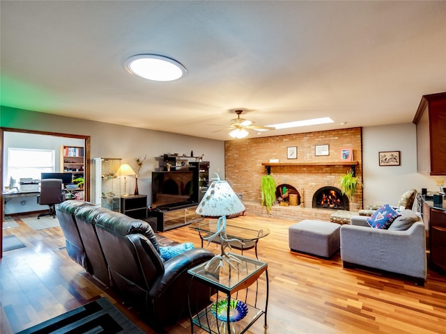 living area with ceiling fan, a fireplace, a skylight, and light wood-style floors