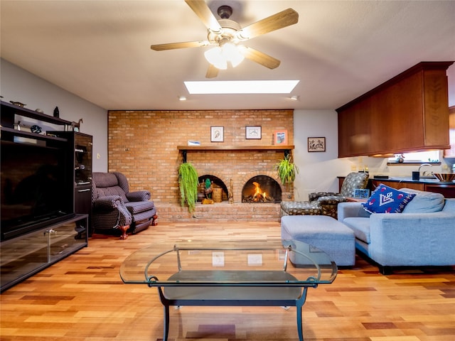 living area with brick wall, light wood finished floors, a brick fireplace, and a skylight