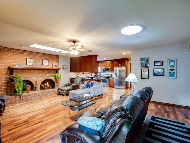 living room featuring light wood finished floors, a fireplace, and a ceiling fan