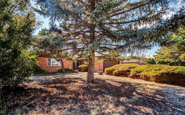 view of property hidden behind natural elements featuring brick siding and an attached garage