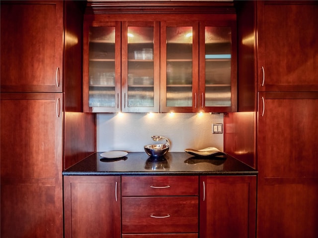 kitchen featuring reddish brown cabinets, glass insert cabinets, and dark stone countertops