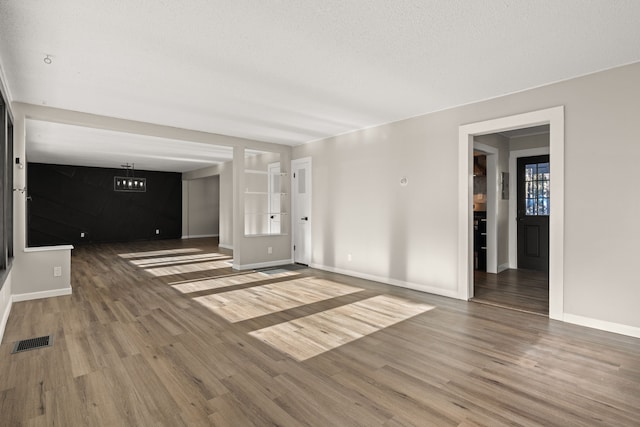 unfurnished living room with baseboards, a textured ceiling, visible vents, and wood finished floors