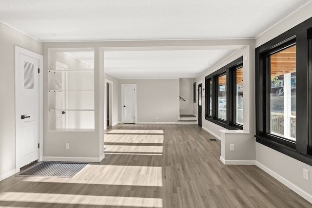 empty room featuring crown molding, wood finished floors, visible vents, and baseboards