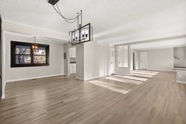 unfurnished living room with a textured ceiling, wood finished floors, visible vents, baseboards, and an inviting chandelier