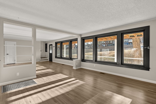 empty room featuring a textured ceiling, wood finished floors, visible vents, and baseboards