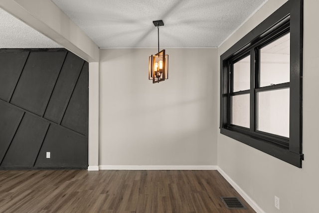 unfurnished dining area with baseboards, visible vents, dark wood-type flooring, a textured ceiling, and a notable chandelier