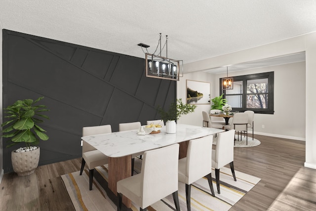 dining area with a textured ceiling, a notable chandelier, a decorative wall, wood finished floors, and baseboards