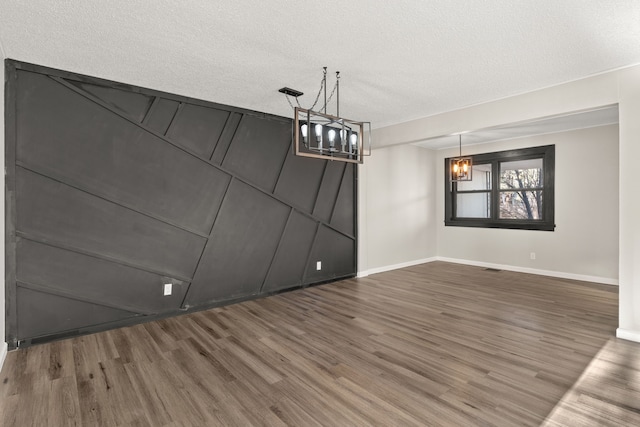 unfurnished dining area with a notable chandelier, a textured ceiling, baseboards, and wood finished floors