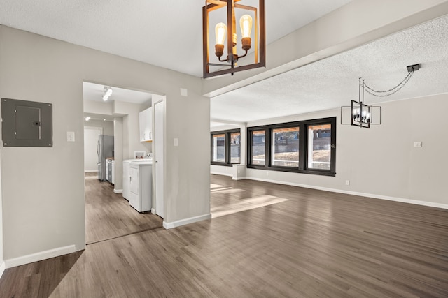 unfurnished living room featuring baseboards, wood finished floors, electric panel, and a notable chandelier