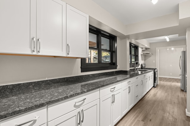 kitchen with light wood finished floors, white cabinets, dark stone counters, wall chimney exhaust hood, and appliances with stainless steel finishes