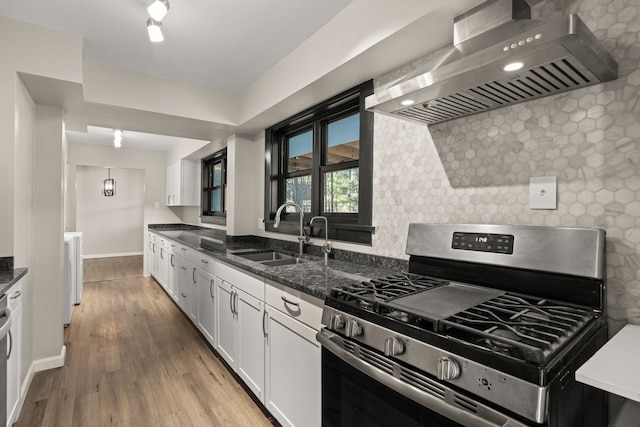 kitchen featuring light wood-style flooring, wall chimney range hood, stainless steel range with gas cooktop, white cabinetry, and a sink