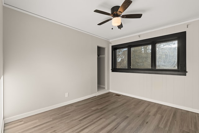 spare room featuring ceiling fan, wood finished floors, visible vents, baseboards, and ornamental molding