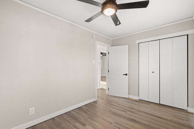 unfurnished bedroom featuring baseboards, a ceiling fan, light wood-style flooring, ornamental molding, and a closet