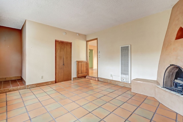 empty room with a textured ceiling, light tile patterned flooring, and baseboards