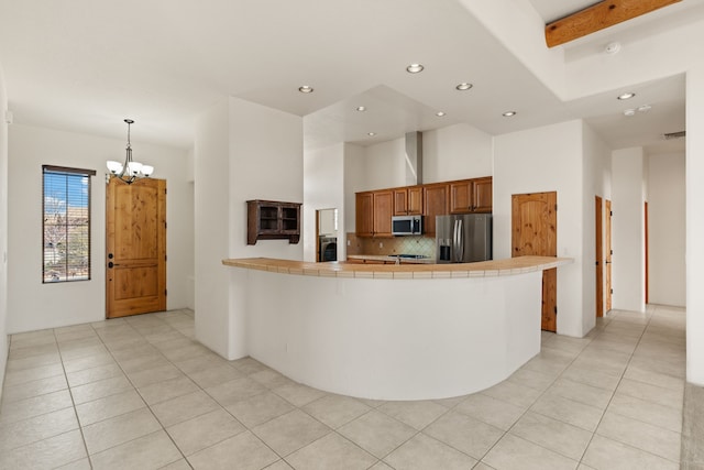 kitchen with light tile patterned flooring, a peninsula, appliances with stainless steel finishes, tile counters, and decorative backsplash