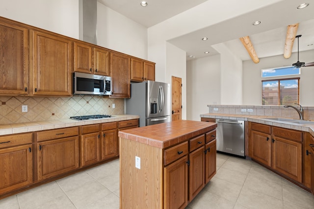 kitchen featuring brown cabinets, decorative backsplash, appliances with stainless steel finishes, a sink, and ceiling fan