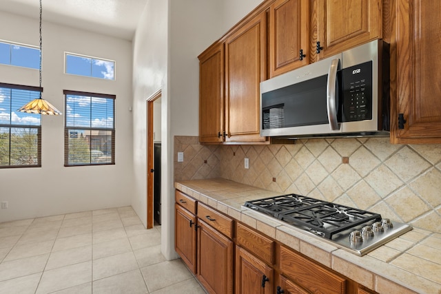 kitchen with brown cabinets, light tile patterned floors, tile counters, backsplash, and appliances with stainless steel finishes