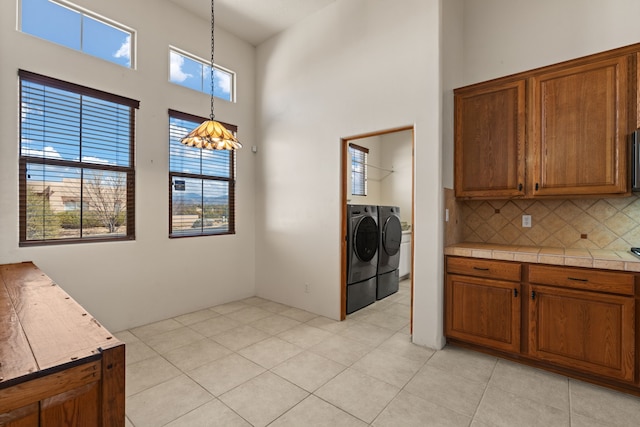 kitchen with brown cabinetry, decorative backsplash, decorative light fixtures, a high ceiling, and separate washer and dryer