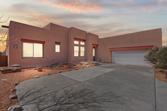 adobe home featuring a garage, concrete driveway, and stucco siding