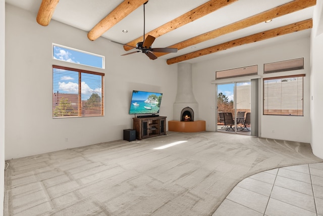 unfurnished living room featuring a ceiling fan, a wood stove, a high ceiling, carpet flooring, and beam ceiling