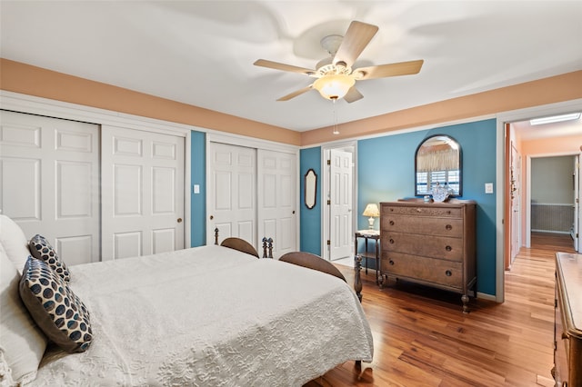 bedroom with a ceiling fan, baseboards, light wood finished floors, and two closets