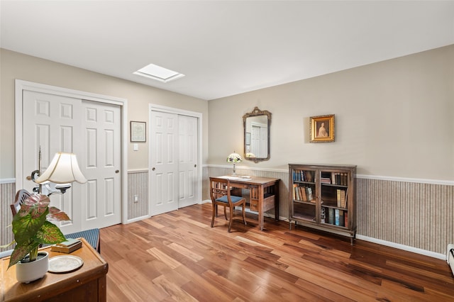 office area featuring wood finished floors, wainscoting, a skylight, and a baseboard radiator