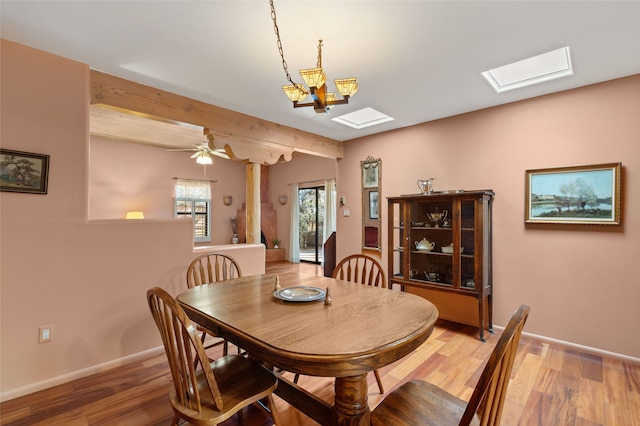 dining room with a skylight, beam ceiling, baseboards, and wood finished floors