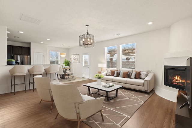 3036 Floras Del Sol St, Santa Fe, NM 87507 - living room featuring a notable chandelier, a large fireplace, recessed lighting, wood finished floors, and visible vents