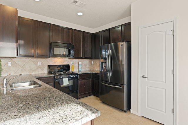 kitchen featuring light stone counters, a sink, visible vents, backsplash, and black appliances