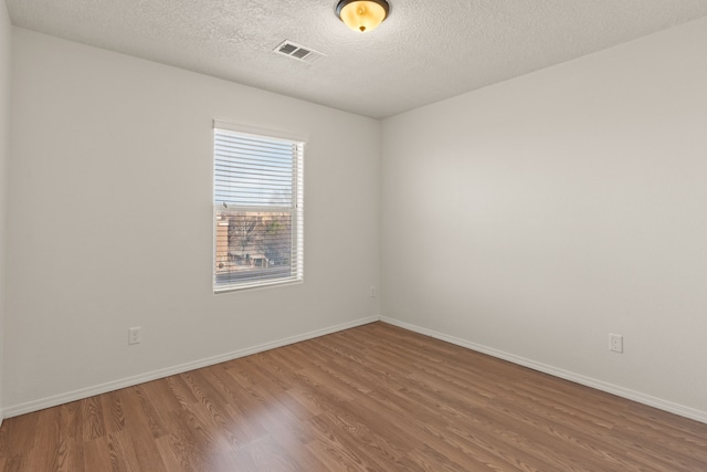 spare room featuring baseboards, a textured ceiling, visible vents, and wood finished floors